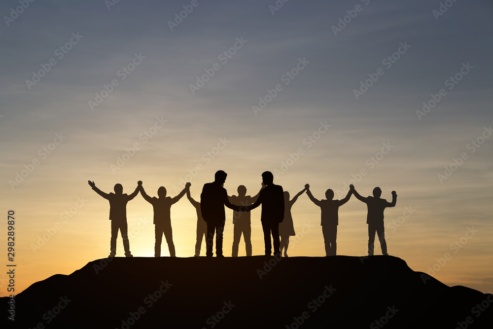 Silhouette of people are celebrating success at the top of the mountain, sky and sun light background. Team business concept.