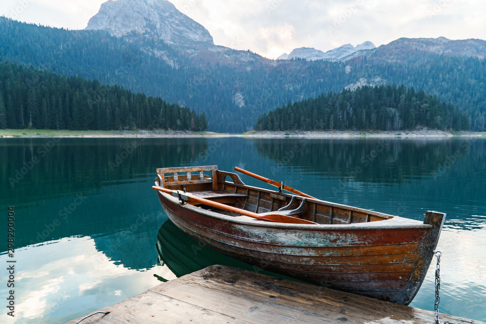 Mountain lake with coniferous forest, a wooden boat and a pier in the frame. Romantic tourist place. National Park Durmitor, Montenegro, Europe.