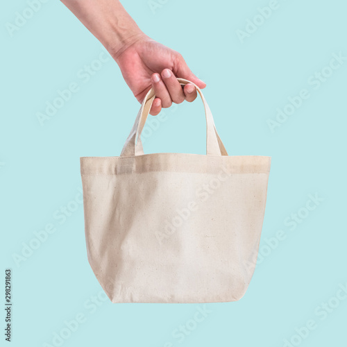 Tote bag canvas white cotton fabric cloth for eco shoulder shopping sack mockup blank template isolated on blue background (clipping path) with woman’s hand handling handle straps