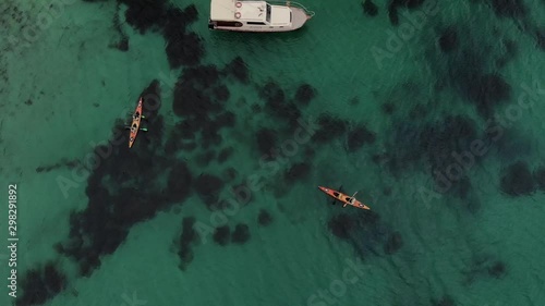 Aerial view travelers on kayak paddling around yacht in crystal lazur sea tith reefs photo