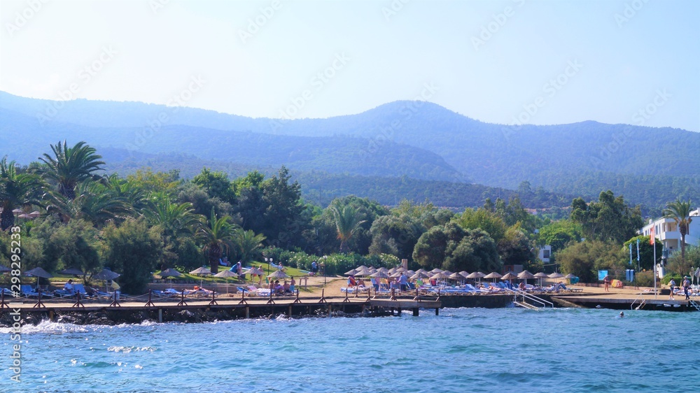  the shore of the blue sea, in the background, vacationers, mountains, hills