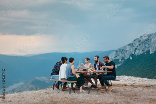 Friends and family gathered for picnic dinner for Thanksgiving. Festive young people celebrating life with red wine, grapes, cheese platter, and a selection of cold meats