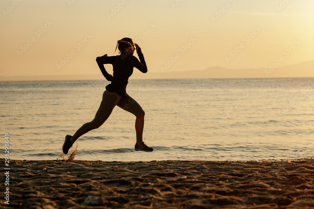 Full length of athletic woman running at the beach at sunrise. Full length of athletic woman running at the beach at sunrise.