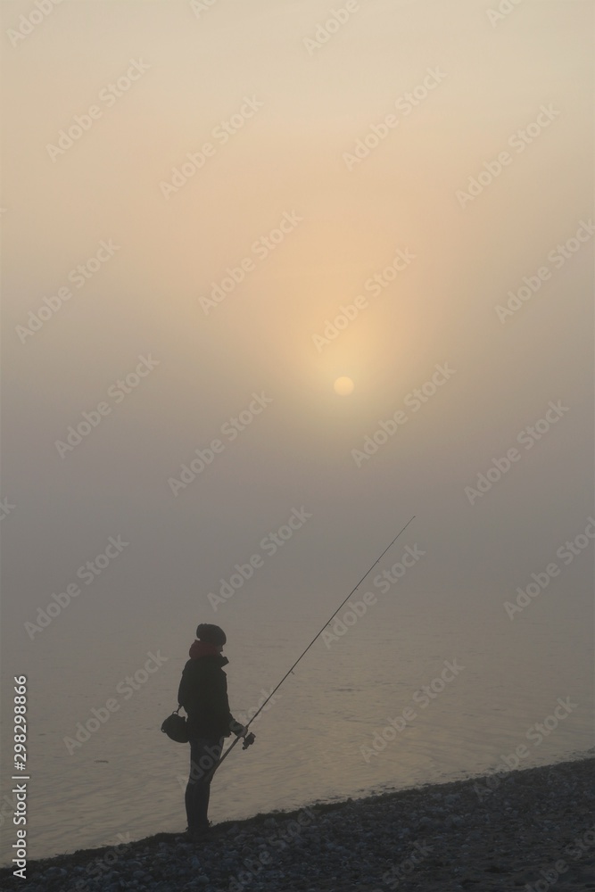 woman with fishing rod in the fog by the sea
