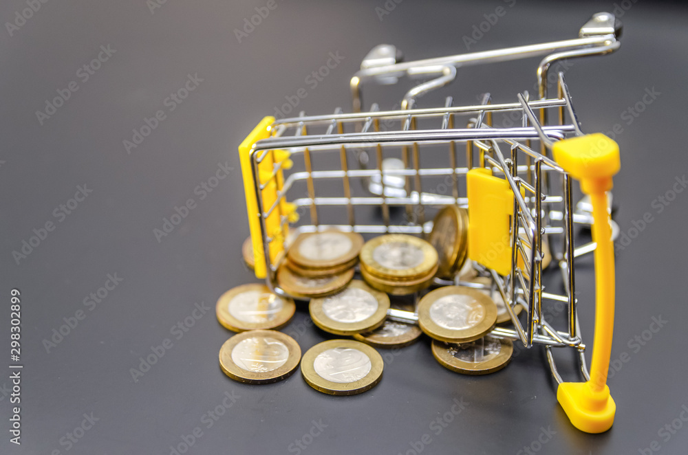 Gold coins scattered from a yellow shopping cart on a black background close up