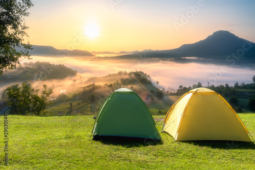 Small Yellow and Green Camping Tent Picnic on green lawn behind mountain sunrise morning sky background, Recreation and outdoor travel concept.