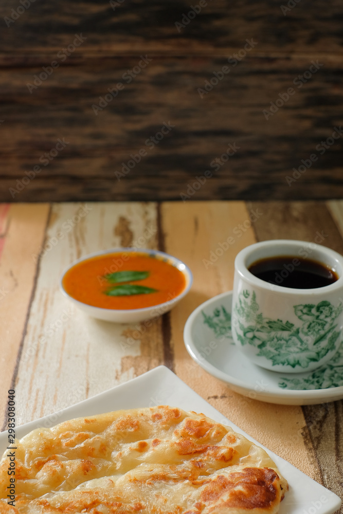 A cup of hot coffee , Roti canai or Roti Parata , dalca and curry sauce on wood background A cup of hot coffee , Roti canai or Roti Parata , dalca and curry sauce on wood background