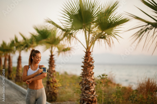 Happy sportswoman adjusting her smart phone while exercising outdoors.