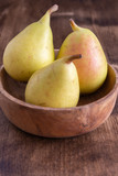 Top view of small pears in wooden bowl on dark wooden board with unfocused background, vertical