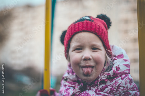 cheerful girl shows tongue while sitting on a swing © Dmitrii