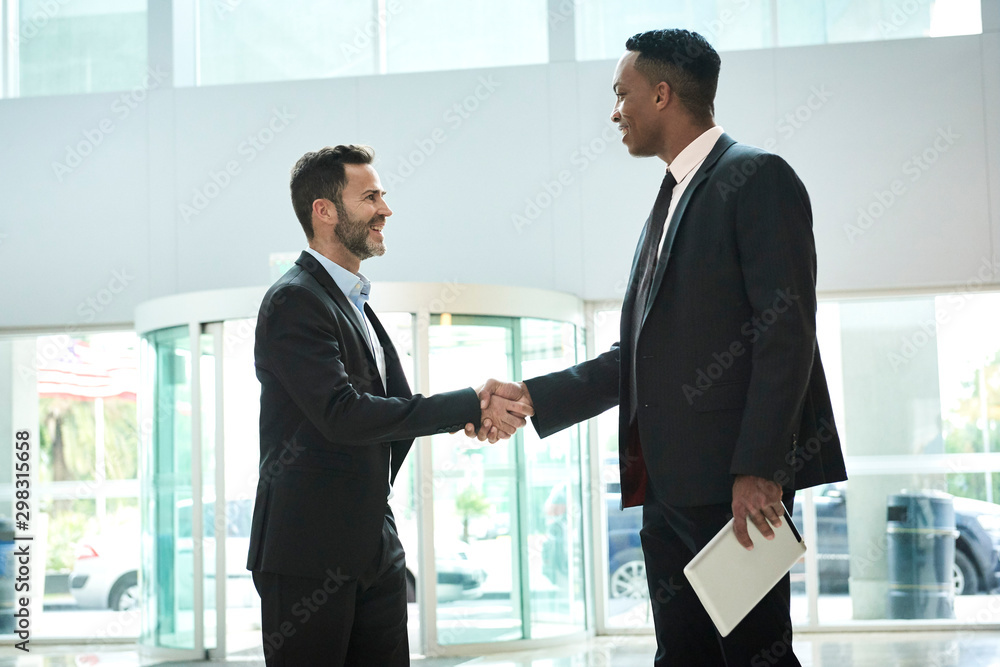 Businessmen shaking hands while standing in office lobby Businessmen shaking hands while standing in office lobby
