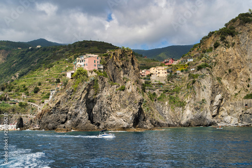 Ligurian coast, mountain and village views on a hill, rocky beach, boat on the water, Manarola, Italy