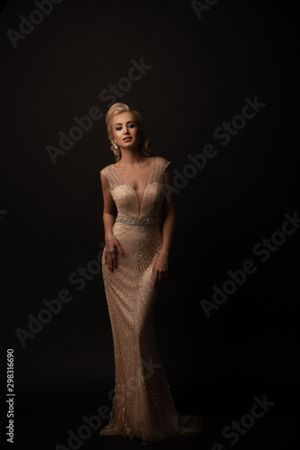 Girl in a dress on a black background. Dress with rhinestones and beads. Hands on hips. Hairstyle and makeup.