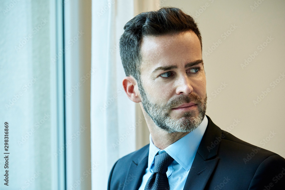 Thoughtful businessman standing near hotel window Thoughtful businessman standing near hotel window