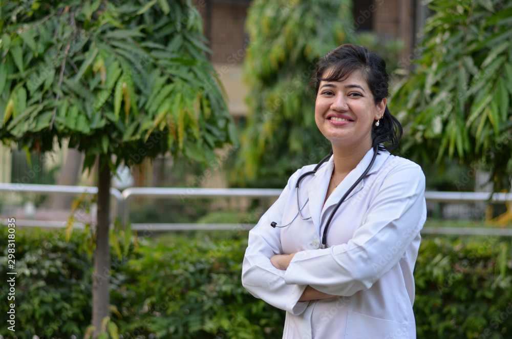 Portrait of a confident young female professional doctor wearing white coat and stethoscope in an outside setting in a park or hospital lawns in New Delhi, India Portrait of a confident young female professional doctor wearing white coat and stethoscope in an outside setting in a park or hospital lawns in New Delhi, India