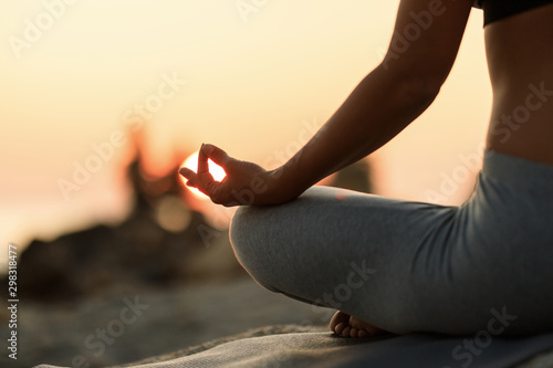 Close-up of woman meditating in lotus position at sunset.