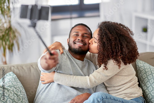 family  technology and people concept - happy african american couple taking picture by smartphone and selfie stick at home