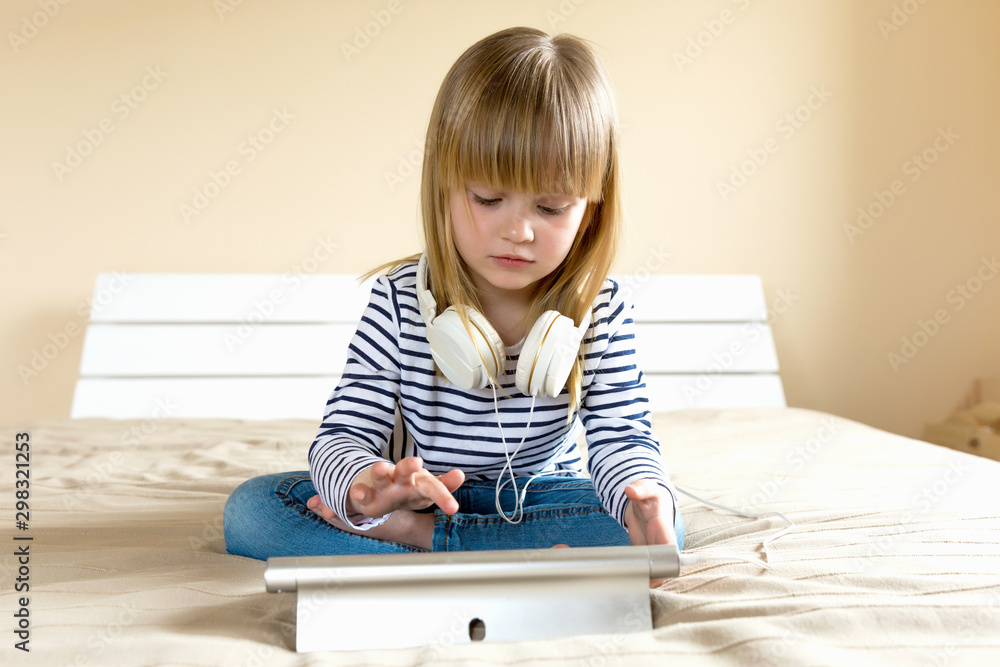 Little blond girl streaming online on tablet with headset. Little blond girl streaming online on tablet with headset.