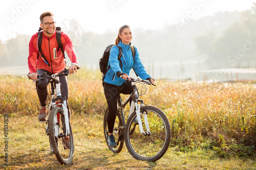 Beautiful happy young couple enjoying early morning bicycle ride by the river or lake. Sunrise through the mist above water in the background photo
