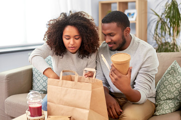 eating and people concept - happy african american couple with takeaway food and drinks at home