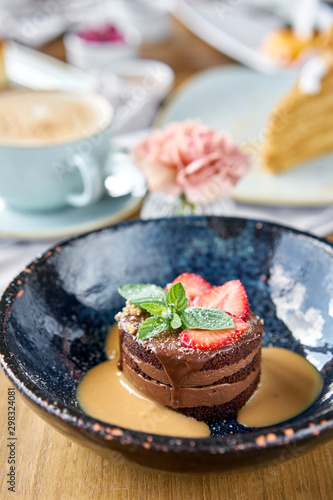 Chocolate sponge cake  with caramel  decorated with strawberries and mint leaf. Breakfast in the cafe  morning coffee. Cappuccino and lots of desserts on the table.