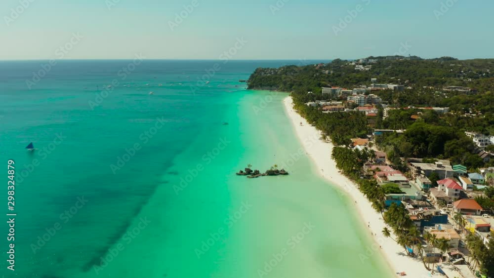 White Beach of Boracay and people swim at turquoise azure sea near Grotto Willy's Rock upon which stands the Virgin Mary Statue. Copy space for text. Summer and travel vacation concept.