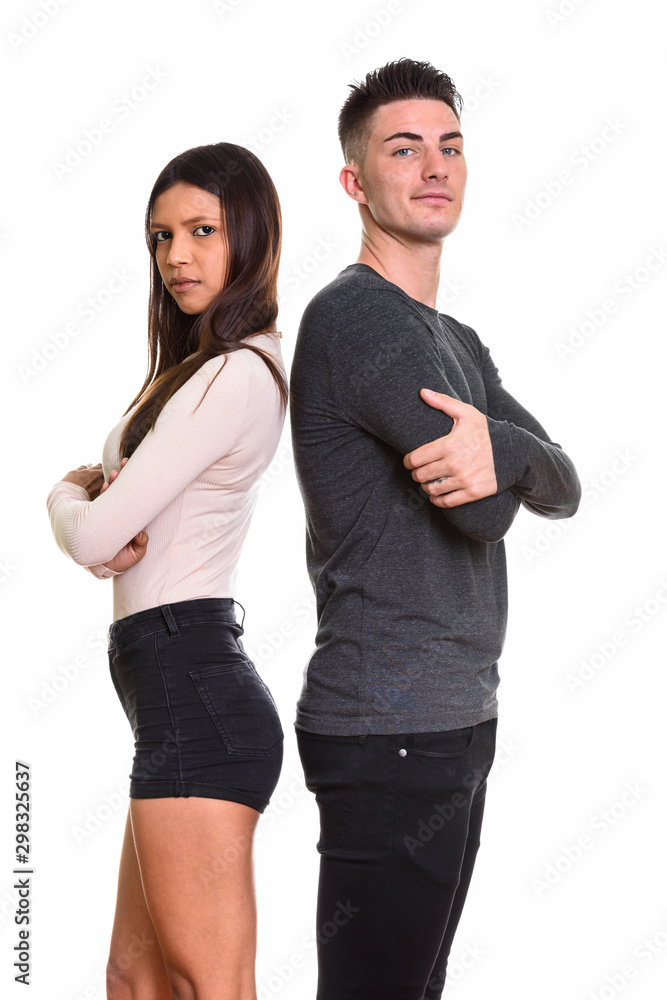 Studio shot of young couple standing back to back with arms cros Studio shot of young couple standing back to back with arms cros