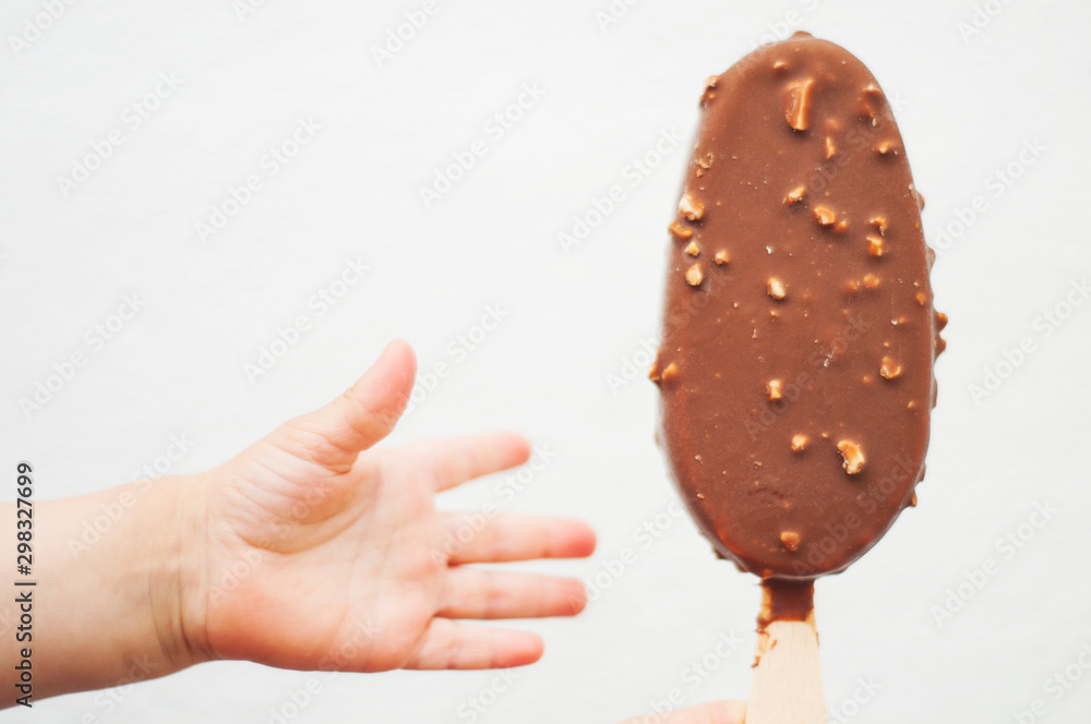 Obraz premium Small baby's hand reaching for the ice cream on a stick. Chocolate ice cream with nuts on white background..