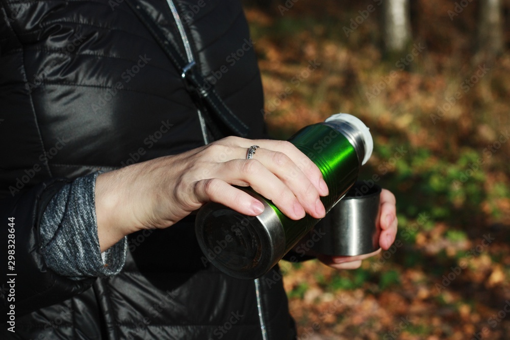 Naklejka premium Woman pours tea from a thermos in the woods