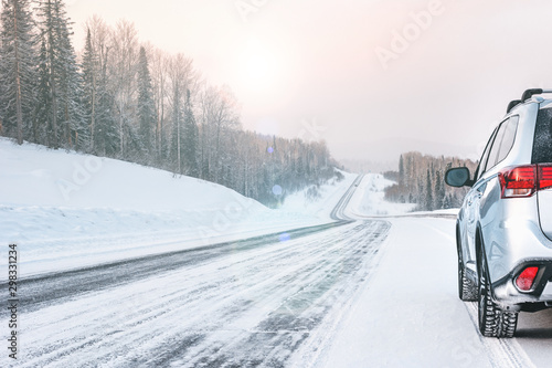 Silver Suv car stay in sunny day on roadside of winter road. Family trip to ski resort. Winter holidays adventure. car on winter snowy road in mountains. Empty winter Road going beyond the horizon
