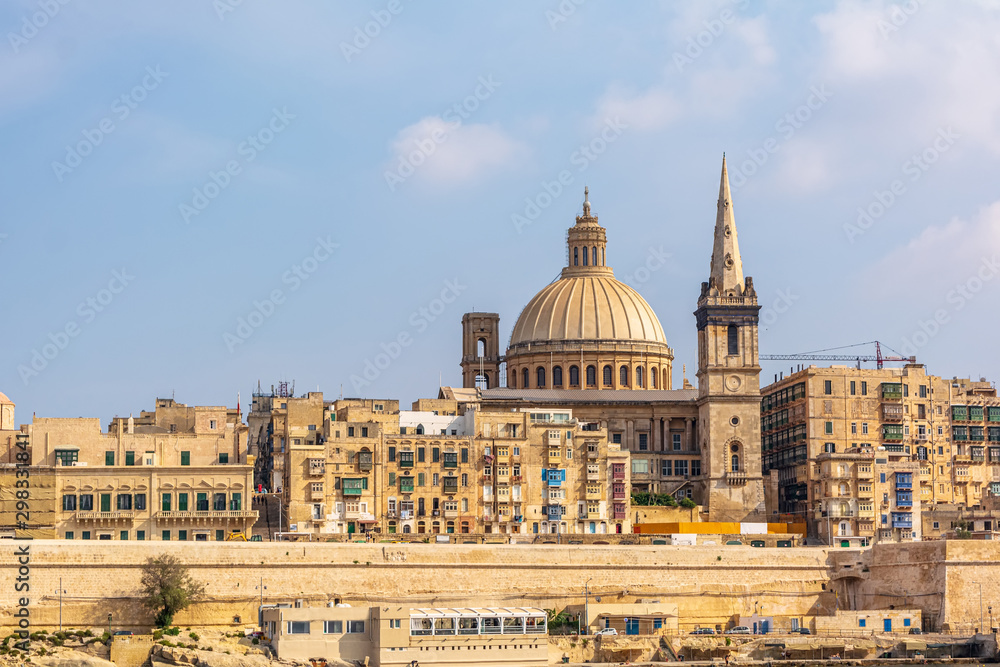 Coastal landscape of Valletta at sunny summer day, with its traditional architecture of yellow limestone. Maltese Valletta skyline with church of Our Lady of Mount Carmel and St Paul's Pro-Cathedral.