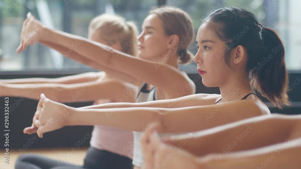 Young diversity sporty people practicing yoga lesson with instructor. Multi racial group of women exercising healthy lifestyle in fitness studio. Sport activity, gymnastics or ballet dancing class.