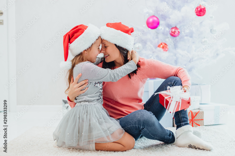 Obraz premium Caucasian mum and daughter are exchanging gifts on Christmas Eve. They are hugging one another and touching with noses.