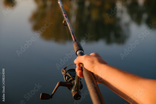 Close-shot of human hands holding a fishing-rod on the foreground