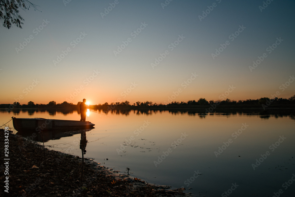 Silhouette of a fisherman. A man catches a fish by the river at sunset.