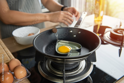 Hands breaking an egg into heart block in a pan