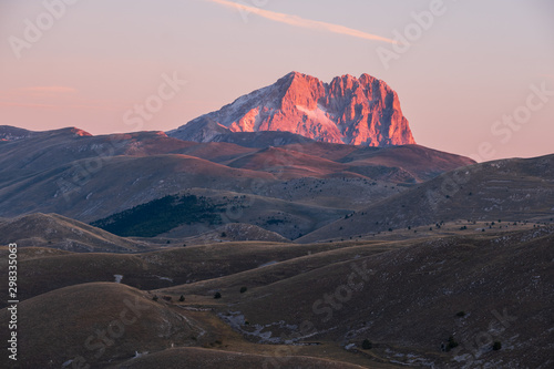 Slika na platnu Mountain Corno Grande on horizon behind barren and rural landscape glowing pink