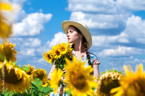 Young beautiful woman in a straw hat in a field of sunflowers