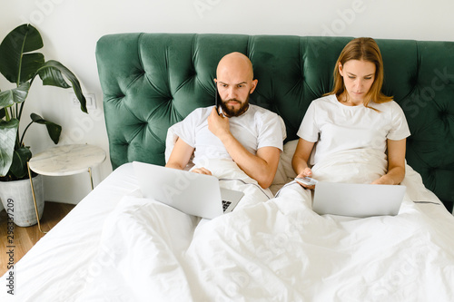 young couple using laptop together in bed 
