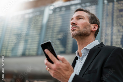 Portrait of businessman with cell phone at arrival departure board at the airport