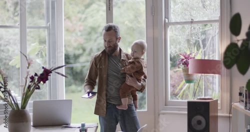 Single parent working from home on smart phone and holding baby