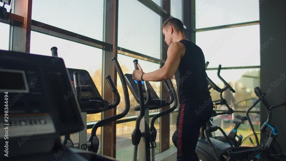 Portrait fitness man warm up before training on elliptical cross trainer in gym club. Close-up male training cardio exercise on cross trainer in fitness. Portrait fitness man warm up before training on elliptical cross trainer in gym club. Close-up male training cardio exercise on cross trainer in fitness.