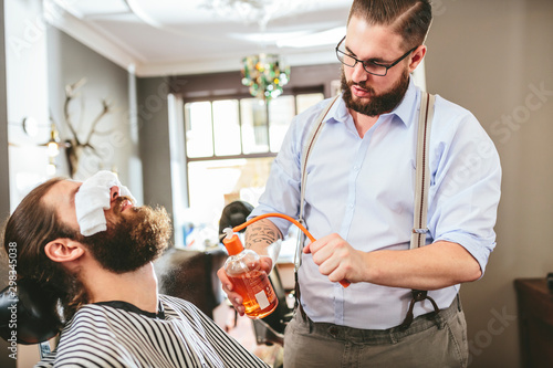Barber spraying aftershave on beard of a customer photo