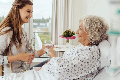 Granddaughter visiting grandmother in hospital, giving her glass of water