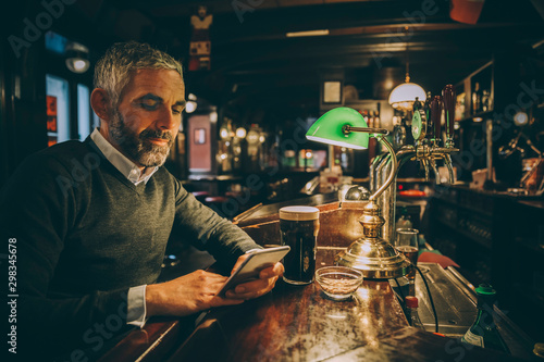 Man sitting at counter of a pub using smartphone photo