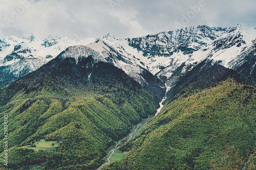 Beautiful mountain landscape, high snowy peaks, cloudy sky, forest.