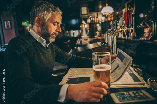 Man sitting at counter of a pub reading newspaper photo