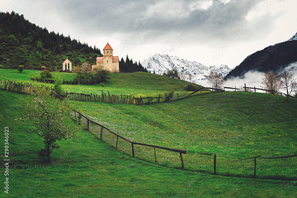 Orthodox Georgian Church in the Caucasus Mountains. Cloudy sky, fog, green grass.