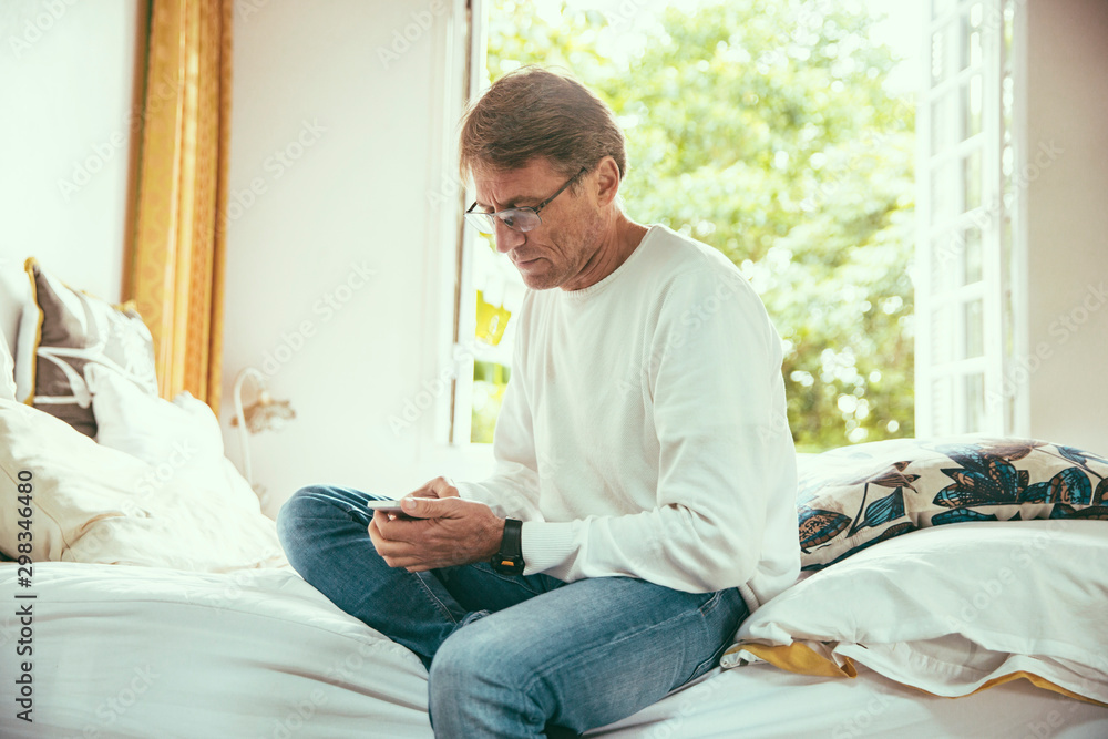 Man sitting on bed looking at his smartphone Man sitting on bed looking at his smartphone