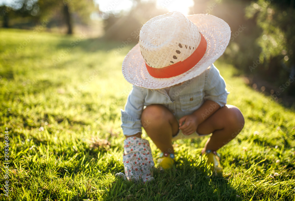 Little girl wearing straw hat crouching on a meadow Little girl wearing straw hat crouching on a meadow